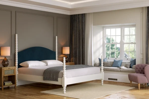 CGI rendering of a stylish bedroom featuring a white four-poster bed with a deep blue upholstered headboard, wooden flooring, bedside tables with lamps, and a window seat with cushions.